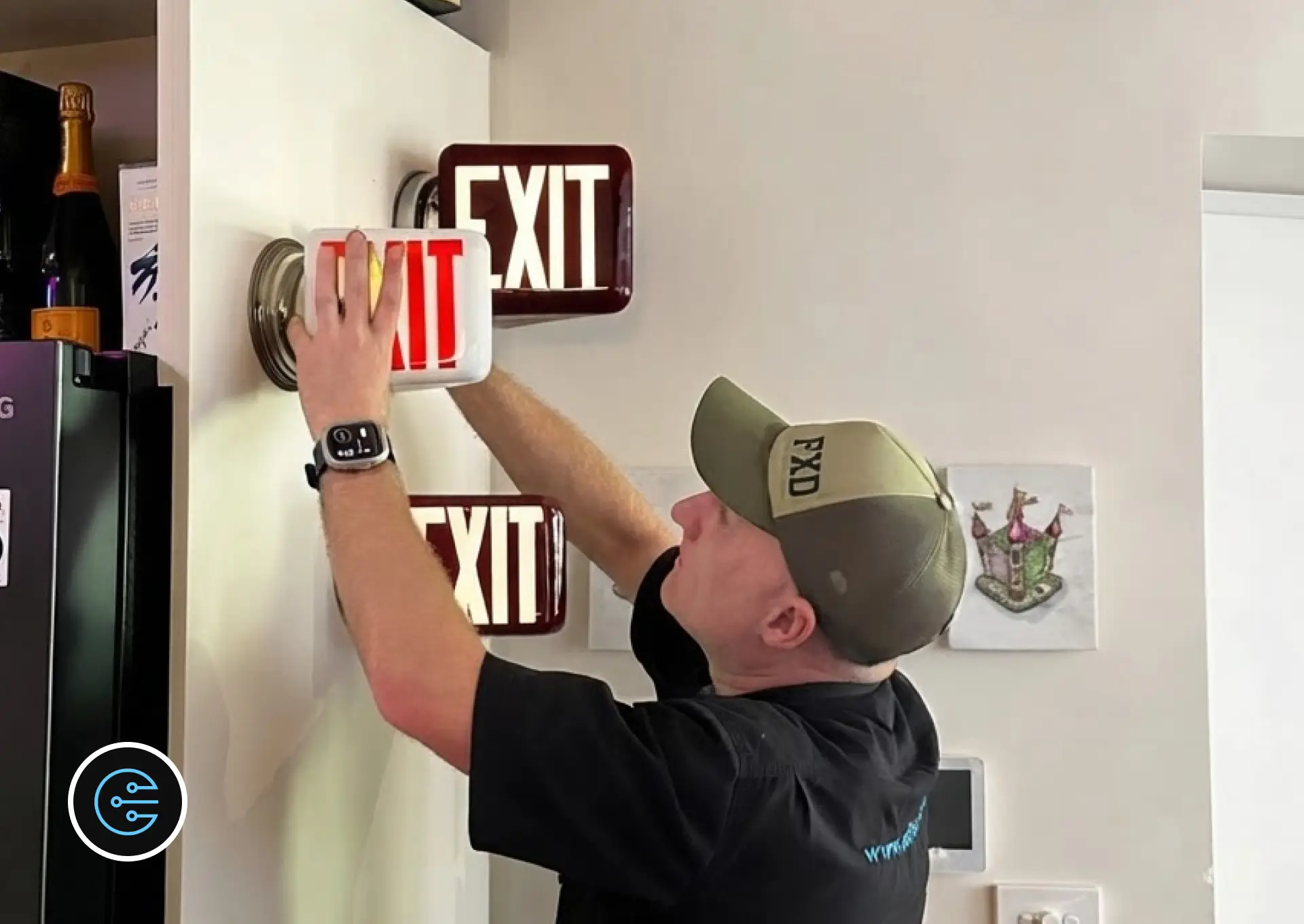 Leonard at All Electrics fitting an antique white glass exit light to a wall beside two maroon exit lights.